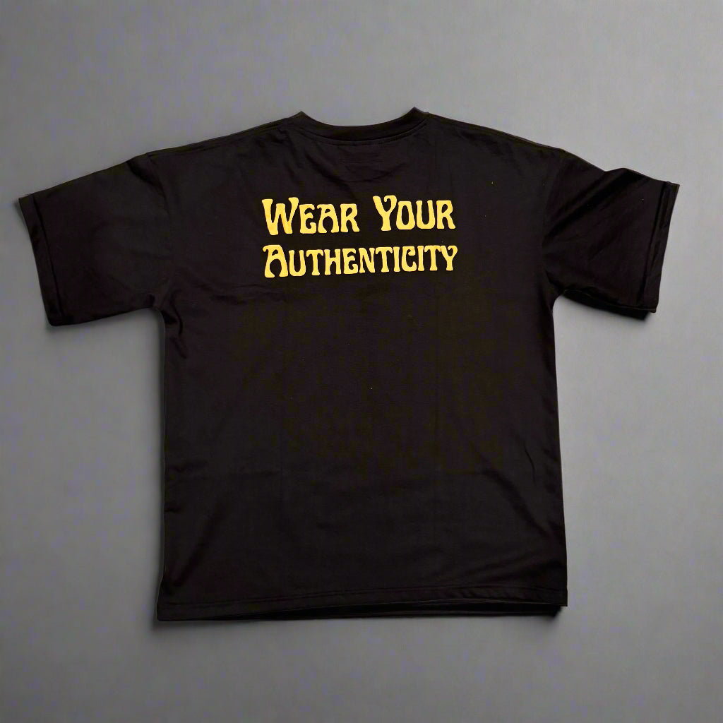 Black t-shirt with 'Wear Your Authenticity' text in yellow on a wooden surface